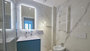 Moderni kylpyhuone, jossa on marmoriseinä, sininen kaappi, valkoinen pesuallas ja wc.
