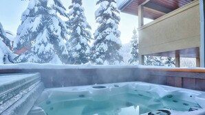 Ett bubbelbad med en trädäck och utsikt över snötäckta träd.