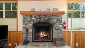 A stone fireplace with a mantel displaying miniature houses, a television on the left, and a fire extinguisher to the right.