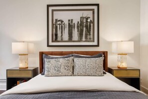 Een hotelkamer met een bed, twee nachtkastjes, twee lampen, een lijst aan de muur en een kussen met een patroon.