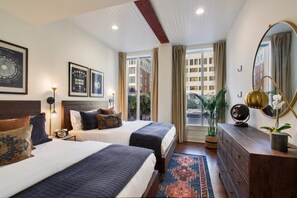A hotel room with two beds, a large mirror, a dresser, and a window with a view of buildings. - Beautiful Renovation | Downtown Savannah (Savannah)