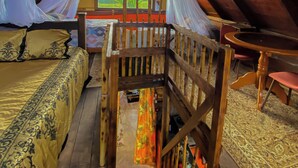 Un dormitorio en el ático con techo de madera, una cama con colcha estampada, una pequeña mesa con sillas y vistas a la vegetación exterior.