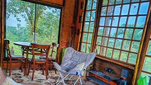 Una habitación acogedora con un sofá de cuero marrón, una mesa de madera con sillas y un ventanal con vistas a la vegetación.