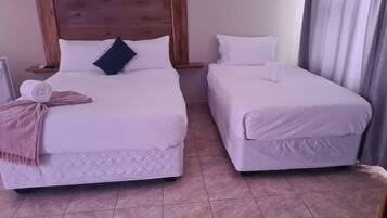 Deux lits simples avec des têtes de lit en bois, une literie blanche et une serviette roulée sur le lit de gauche.