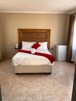 Una cama bien tendida con cabecera de madera, ropa de cama blanca y un plaid rojo.