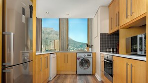 A compact kitchen with wooden cabinets, a built-in washer and dryer, a refrigerator, and a microwave. - Cartwrights Corner 1403 (Cape Town)