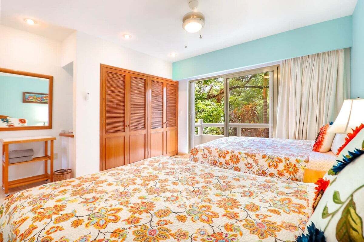 A bedroom with two beds, a wooden wardrobe, a small desk, and a window with curtains.