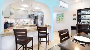 Una cocina moderna con armarios blancos, una isla central y una zona de comedor con dos sillas de madera y una mesa.