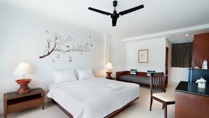 A hotel room with a bed, two bedside tables with lamps, a desk with a chair, a ceiling fan, and a wall with a decorative tree and bird artwork. - Hill Myna Holiday Park & Cafe (Choeng Thale)