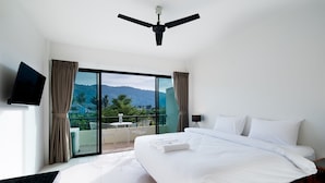 A hotel room with a large bed, a ceiling fan, a TV, and a balcony with a table and chairs. - Hill Myna Holiday Park & Cafe (Choeng Thale)