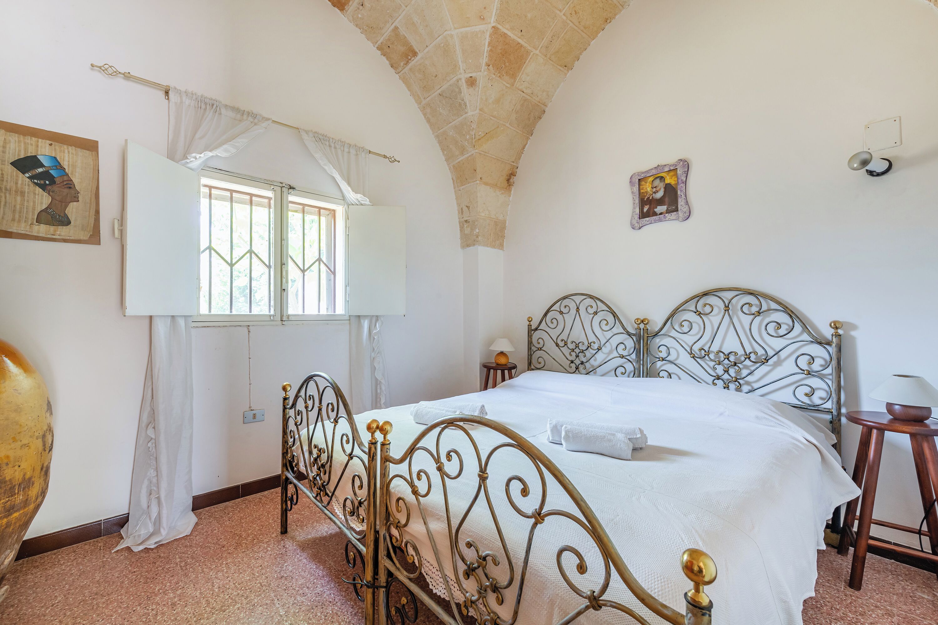 A bedroom with a bed, a window with curtains, a wall-mounted picture, and a stone ceiling.