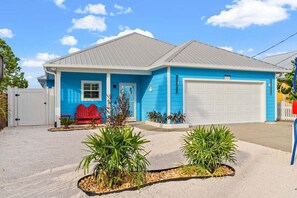A single-story house with a garage, a red bench, and two potted plants in the driveway.