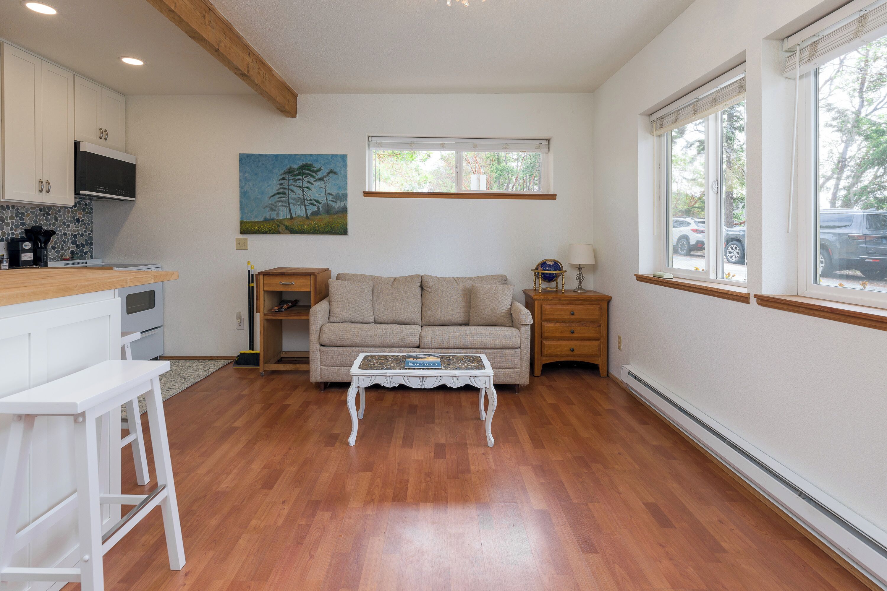 A spacious living area with a wooden floor, a beige sofa, a coffee table, and a kitchen area with white cabinets and a microwave.