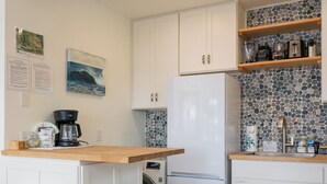 Una cocina con armarios blancos, un refrigerador, una cafetera y una encimera de madera.