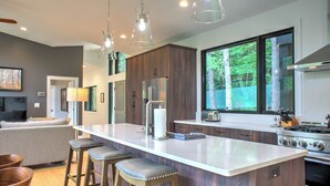 Una cocina moderna con una isla grande, taburetes de bar, electrodomésticos de acero inoxidable y vistas al exterior.