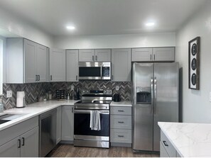 A modern kitchen with stainless steel appliances, white cabinetry, and a herringbone-patterned backsplash.