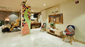 A reception area with a desk, chairs, a teddy bear, and a mosaic wall. - California Hotel (Buan)