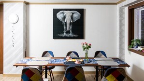 A dining area with a table set for four, a framed elephant artwork on the wall, and a window with a view of the city. - California Hotel (Buan)