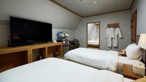 A hotel room with two beds, a TV, a desk with a computer, a mirror, and a wardrobe with robes. - California Hotel (Buan)