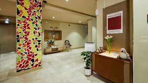 A reception area with a mosaic wall, a wooden reception desk, a potted plant, and a poster on the wall. - California Hotel (Buan)