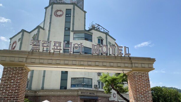 A motel with a prominent sign, brick facade, and outdoor seating area. - California Hotel (Buan)