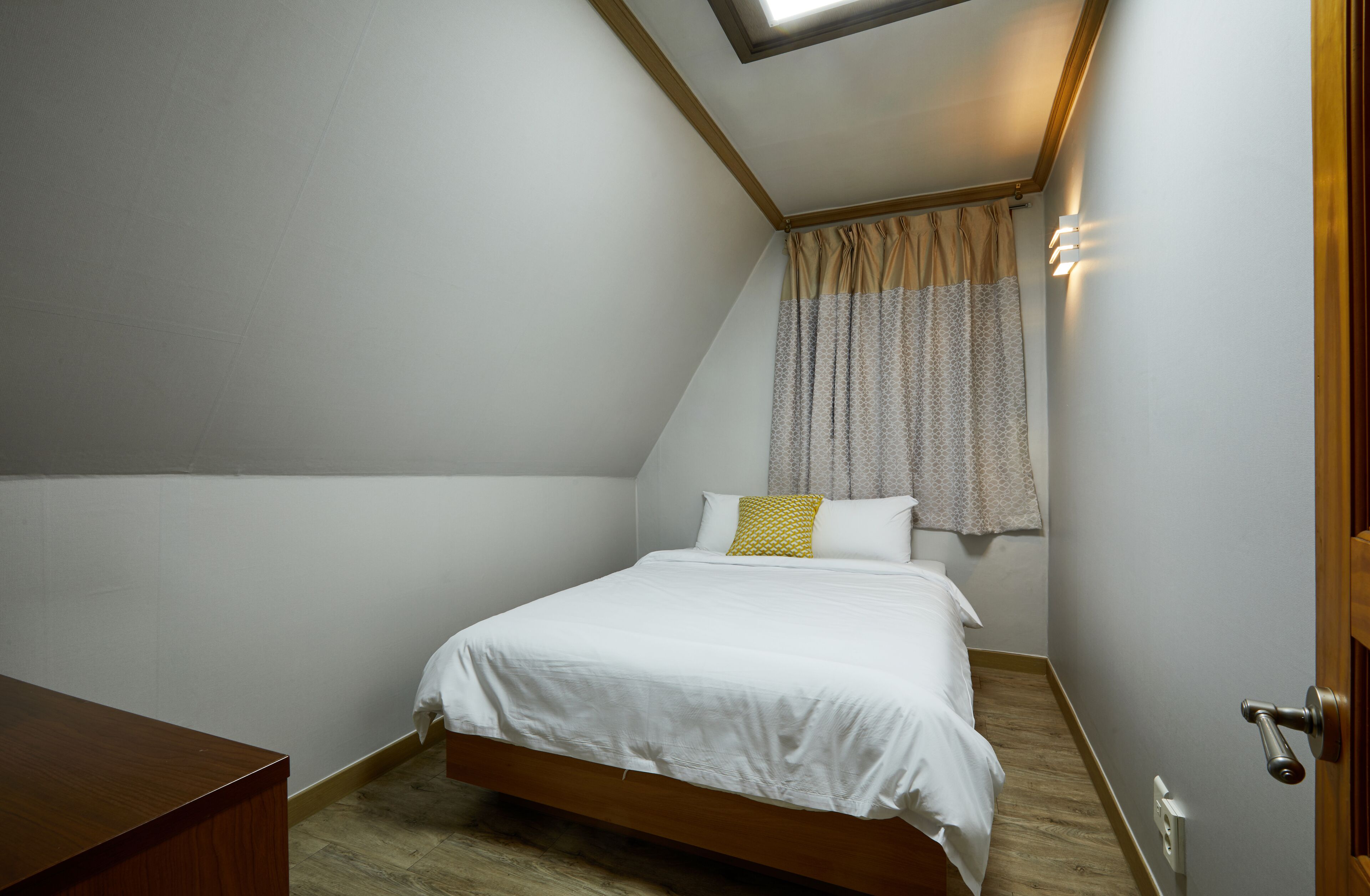 Ein Schlafzimmer mit Bett, einem Holztisch, einem Oberlicht und einem Fenster mit Vorhängen.