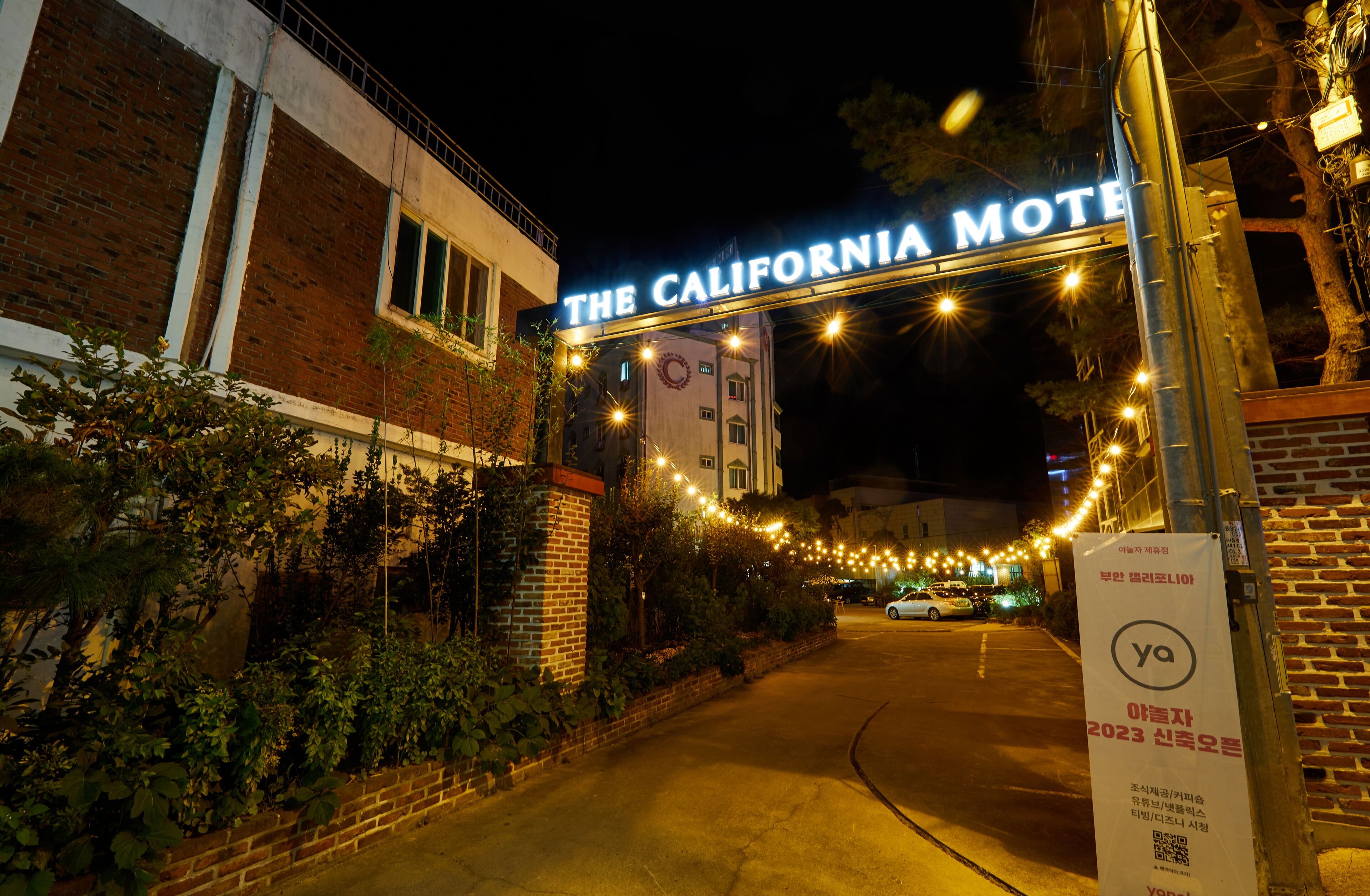 El exterior del California Motel, con un letrero sobre la entrada, un muro de ladrillo y una guirnalda de luces a lo largo del camino.