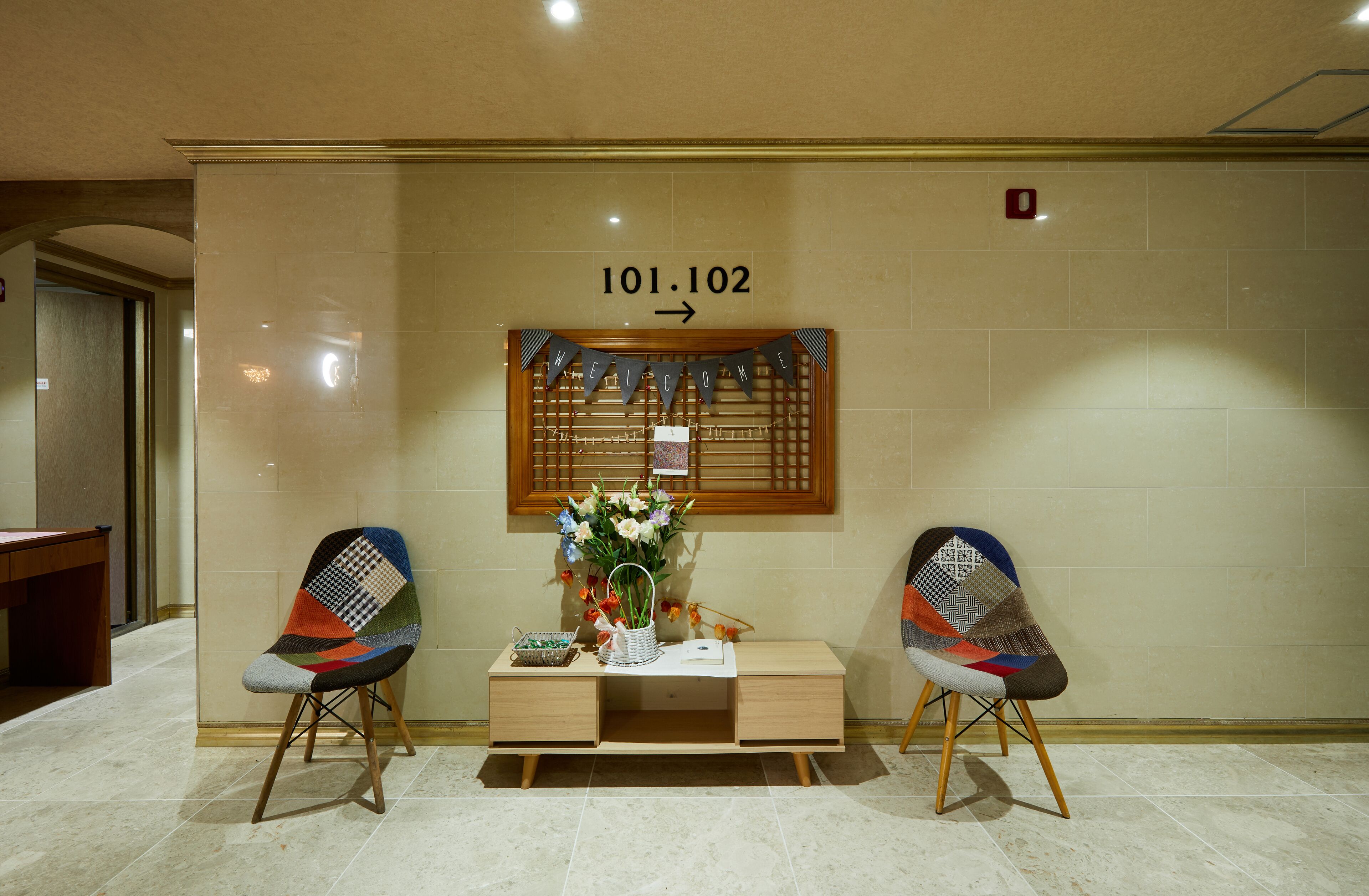 A reception area with a desk, two chairs, a welcome banner, and a sign indicating room number 101.102.