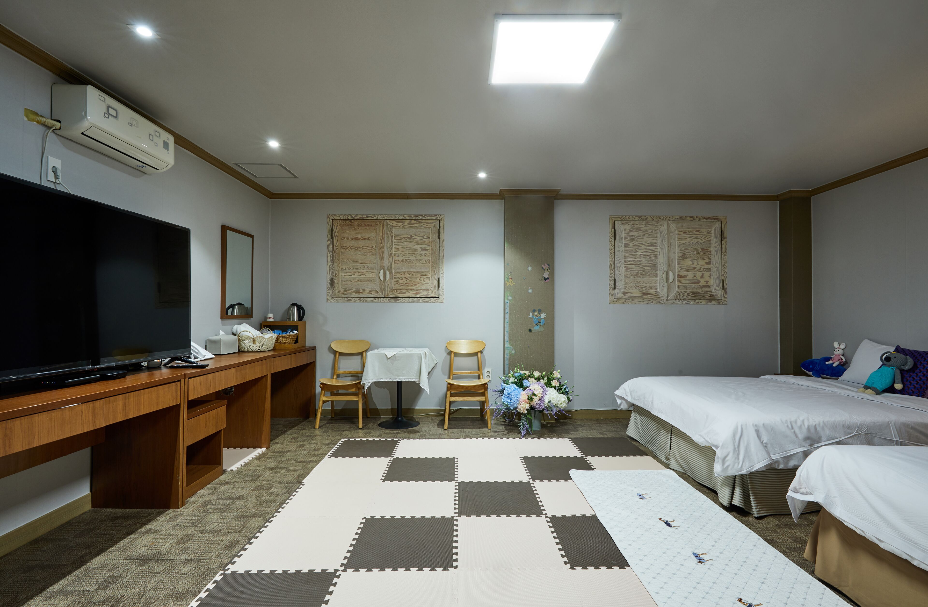 Une chambre d’hôtel équipée d’un téléviseur à écran plat, d’un bureau avec un téléphone, de deux chaises, d’une petite table, d’un lit avec du linge de lit blanc et d’un panneau décoratif mural.