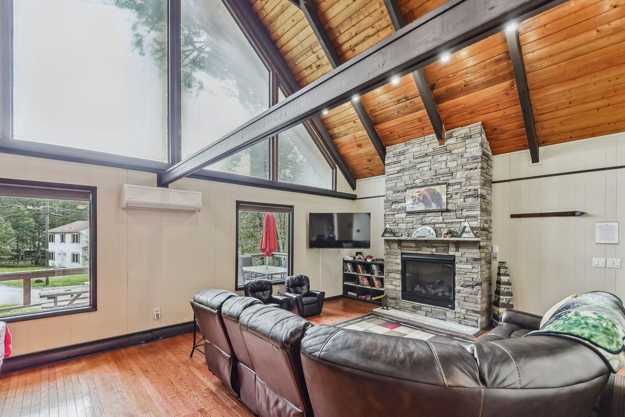 Un salón amplio con chimenea de piedra, asientos de cuero, ventanas grandes y techo de madera.