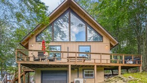 A two-story cabin with a large window, a deck, and a garage. - Poconos Chalet Newly Renovated, Great Location 3 Bedroom Home by RedAwning (Tobyhanna)