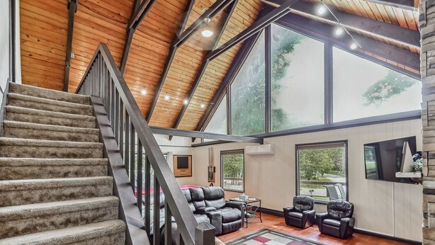 A spacious living area with a high ceiling, large windows, a staircase, and leather seating. - Poconos Chalet Newly Renovated, Great Location 3 Bedroom Home by RedAwning (Tobyhanna)