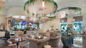 A spacious coffee shop with seating areas, a bar, and a large potted plant.