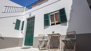 A white building with green shutters, a green door, and a small table with two chairs. - Sandybeachapartment1 in the Golden Island (Vila Baleira)