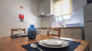 A clean, modern kitchen with white cabinets, a blue vase, two wine glasses, and a dining table set with plates and cutlery. - Sandybeachapartment1 in the Golden Island (Vila Baleira)
