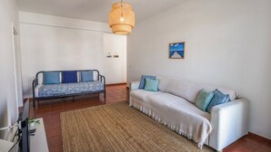 A living room with a sofa, a chair, a TV, and a hanging light fixture. - Sandybeachapartment1 in the Golden Island (Vila Baleira)