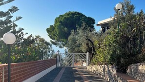 A stone pathway leading to a gate with a view of a large tree and a building. - The perfect place for your dream holiday (Lucerta)