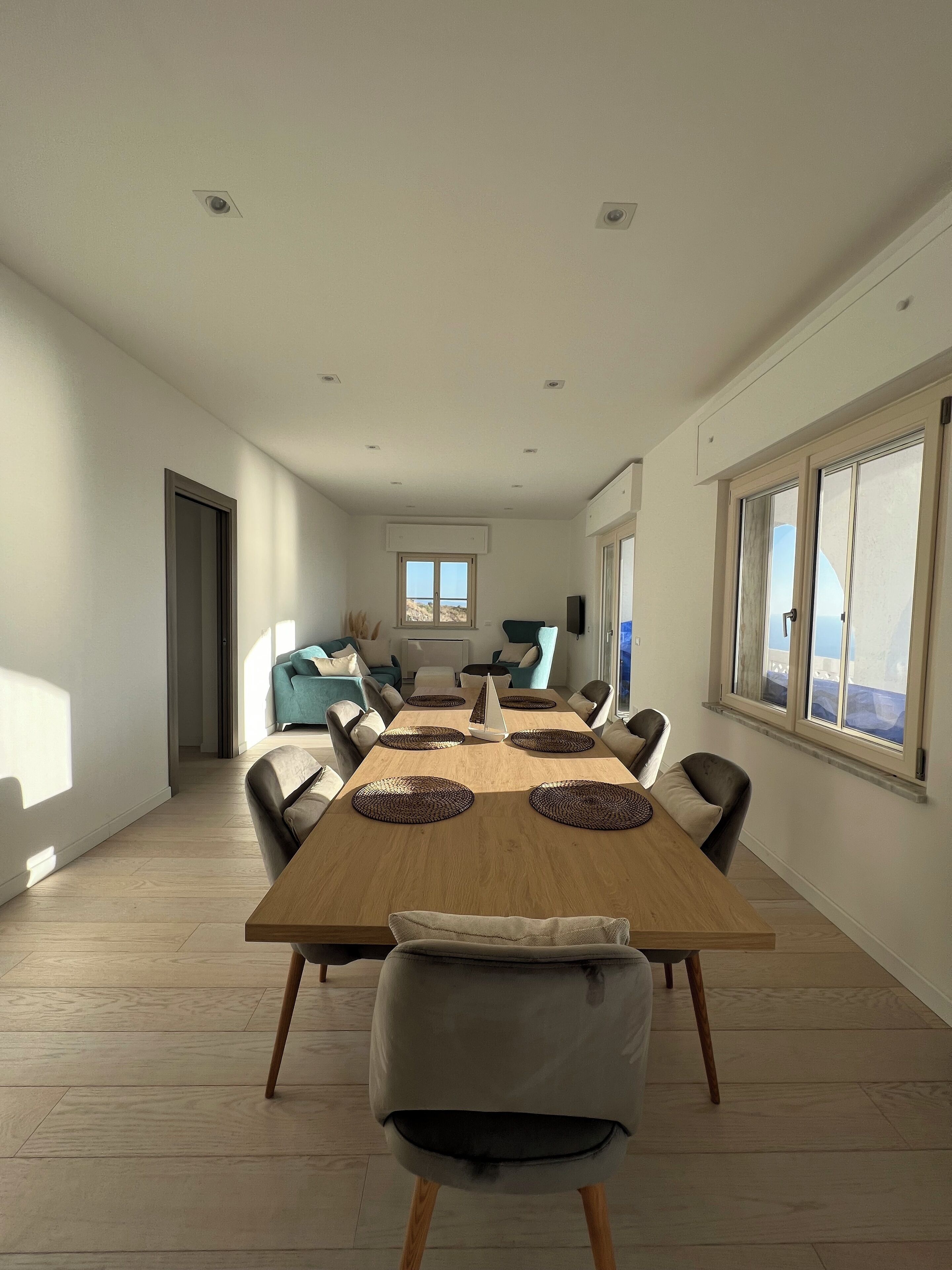 A spacious dining area with a long wooden table, multiple chairs, and a view of the outdoors through large windows.