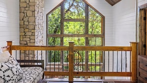 A cozy cabin interior with a stone wall, a large window offering a view of trees, and a wooden bench. - Southern Honey in Hochatown/Broken Bow, OK (Broken Bow)