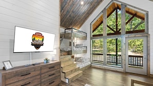 A cabin interior with a large window, wooden staircase, and a flat-screen TV displaying a logo. - Southern Honey in Hochatown/Broken Bow, OK (Broken Bow)