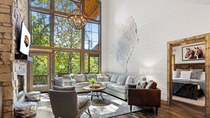 A spacious living room with a stone fireplace, large windows, a leather sofa, and a mounted animal hide. - Southern Honey in Hochatown/Broken Bow, OK (Broken Bow)