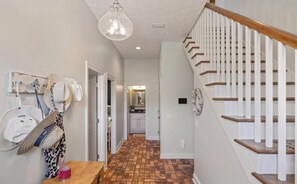 A hallway with a wooden bench, a hanging hat rack, and a staircase with white railings. - Welcome Beach Bum Inn (Panama City Beach)
