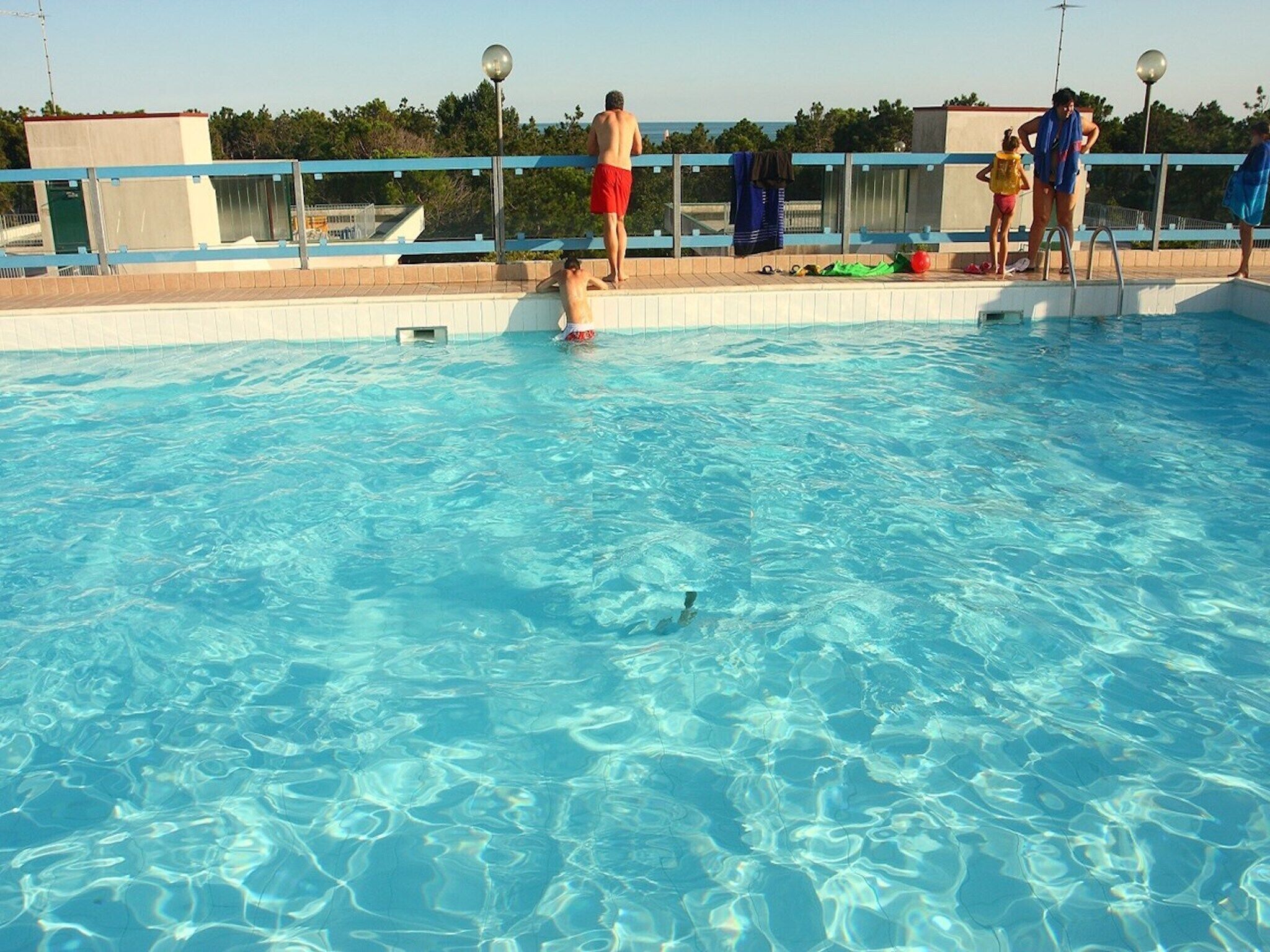 A swimming pool with clear blue water, a tiled deck, and a railing.