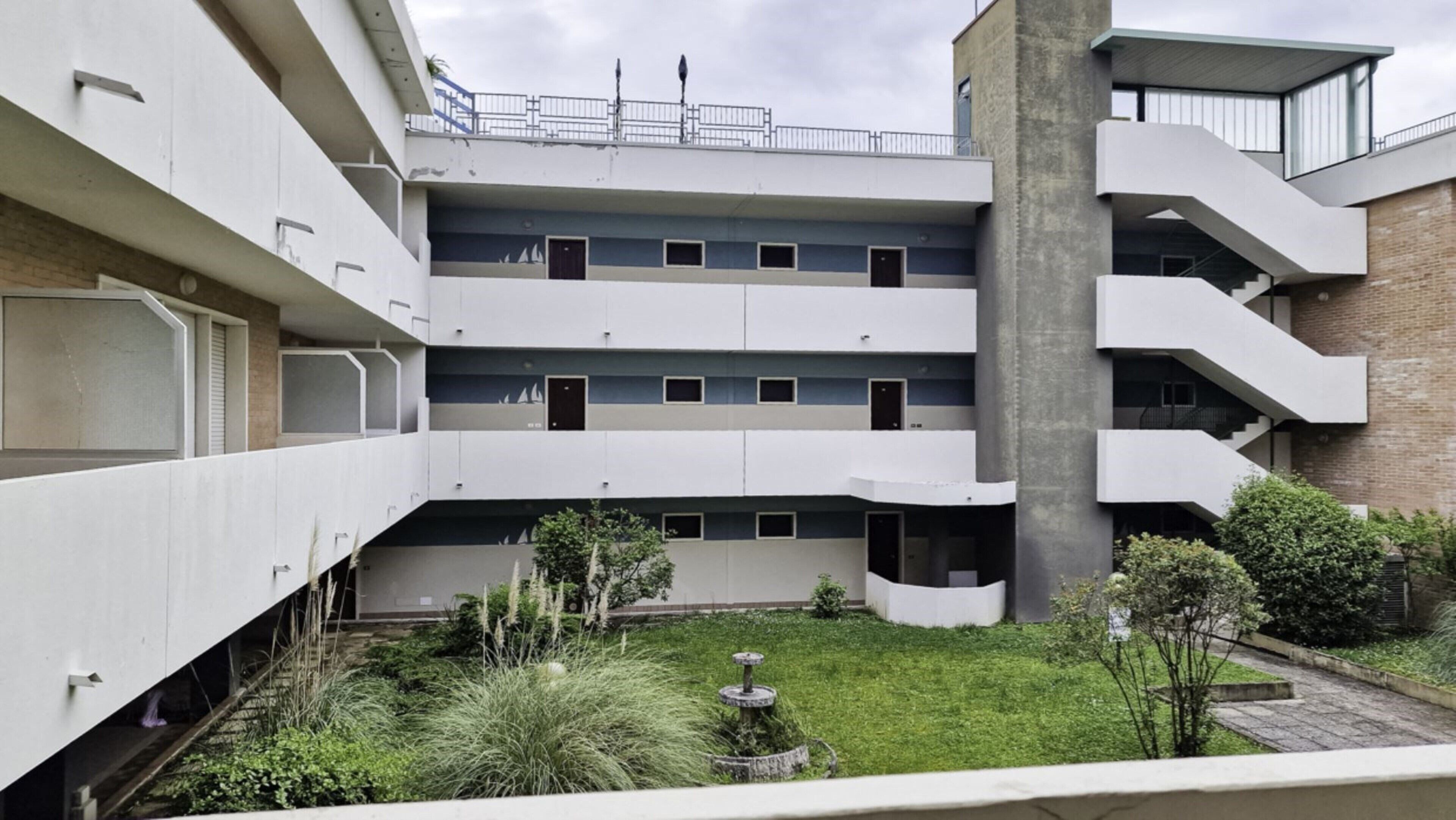 A multi-story building with a courtyard featuring a fountain and greenery.