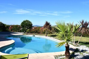 A swimming pool with a curved edge, surrounded by a garden with various plants and flowers, and a clear blue sky in the background. - Magnificent villa with swimming pool and panoramic view in St Gely du Fesc (Saint-Gély-du-Fesc)
