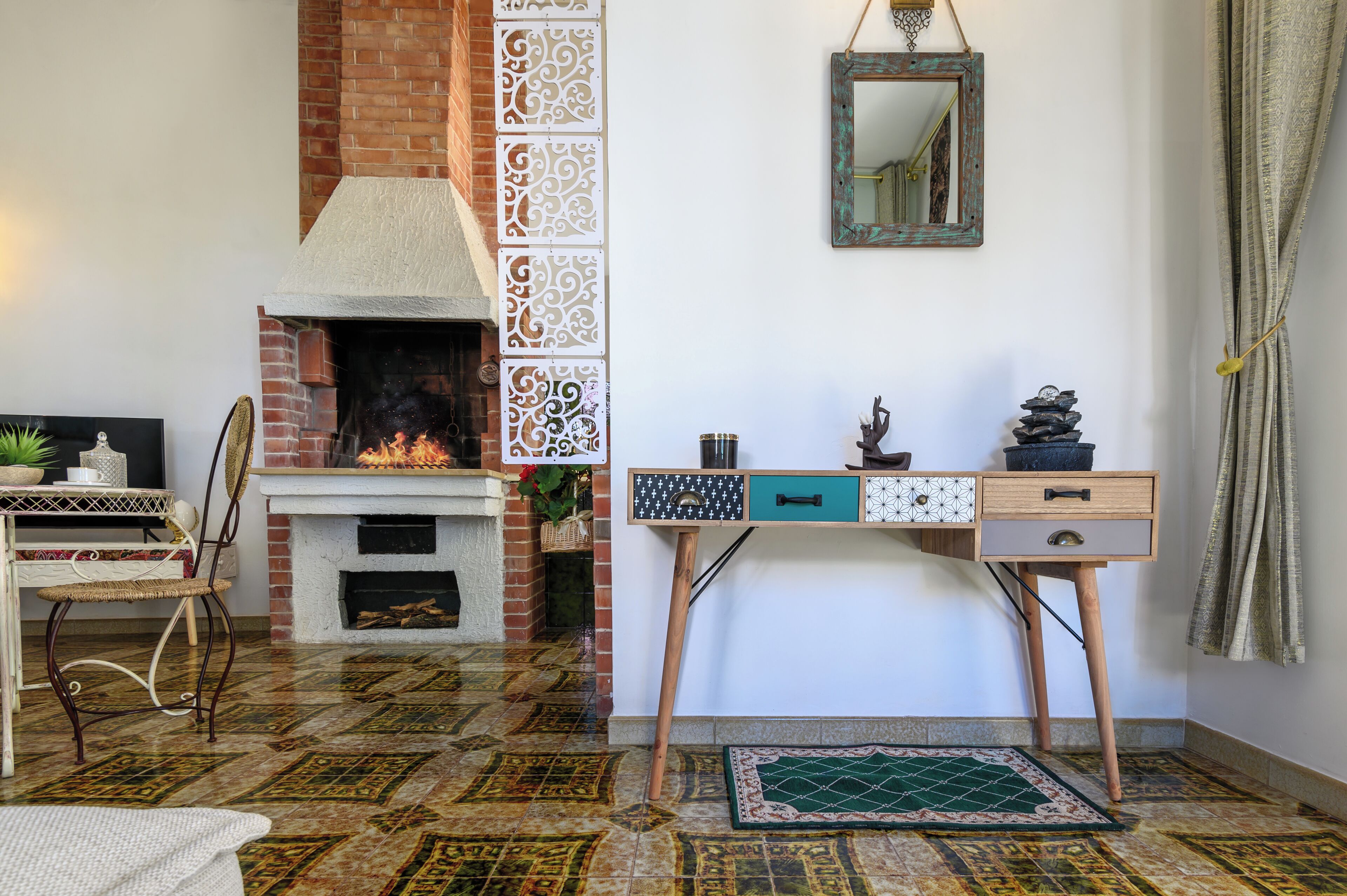 Una habitación con chimenea, un escritorio con cajones, una silla y suelo estampado.