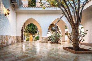 Une cour avec un sol carrelé, des arcades et des plantes en pot.