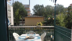 A balcony with a table and chairs, a railing, and a view of buildings and trees. - Homely Flat With Balcony and Swimming Pool (San Michele al Tagliamento)