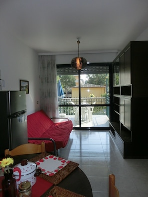 Espaço compacto com cozinha compacta, área de refeições, sofá vermelho e varanda com vista.