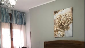 Uma cama bem arrumada com roupa de cama azul e branca, uma cabeceira de madeira e um quadro na parede com flores secas.